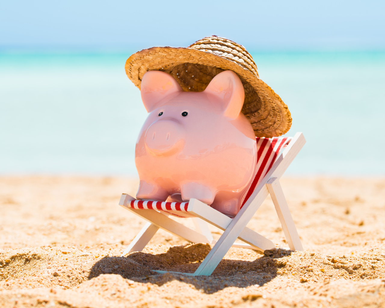Souvenir piggy in hat lies in a toy chair on the beach