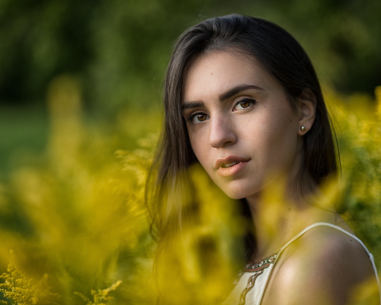 Красивая девушка с нежным взглядом сидит у желтых цветов
