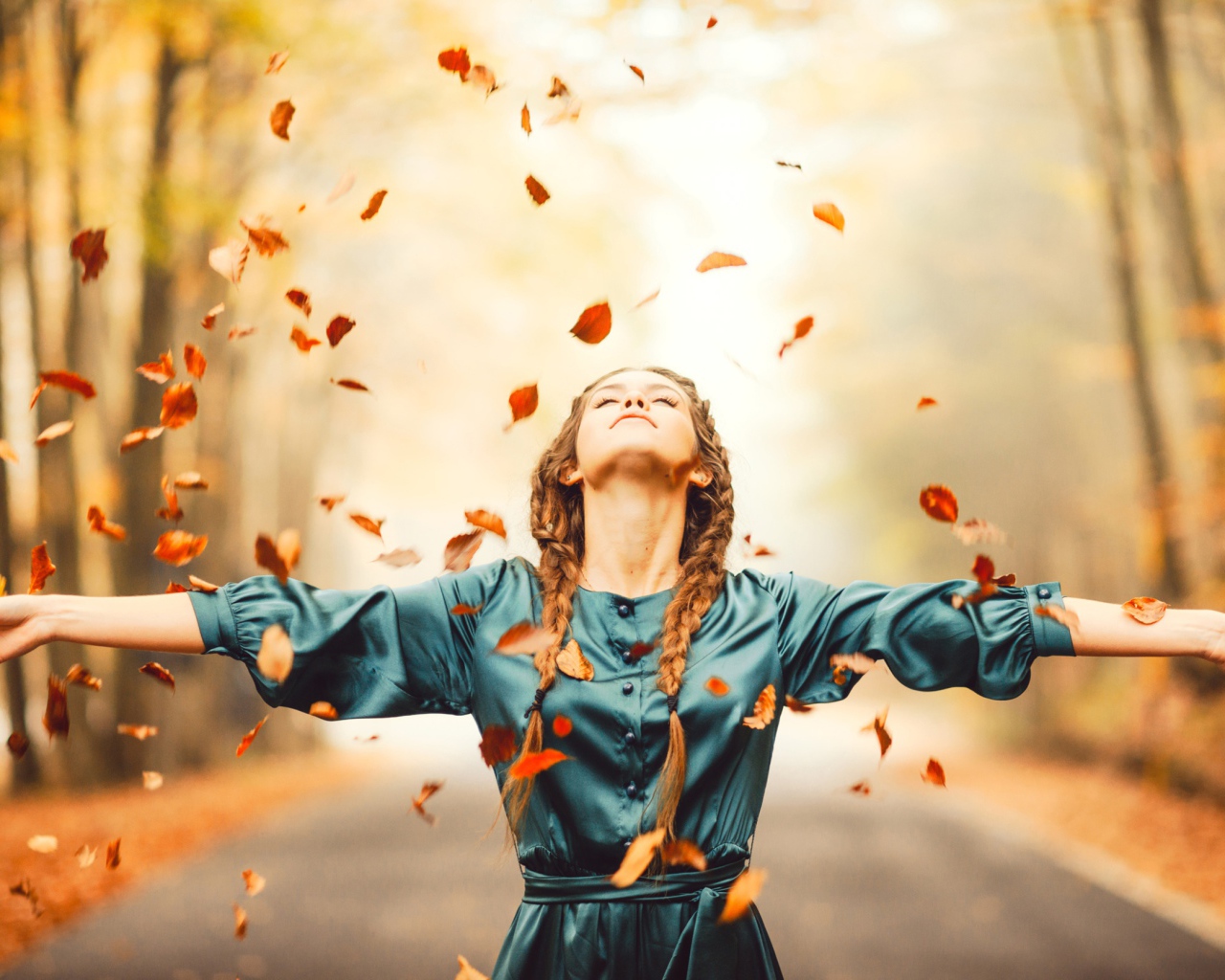 Красивая девушка с косичками подбрасывает желтые листья осенью