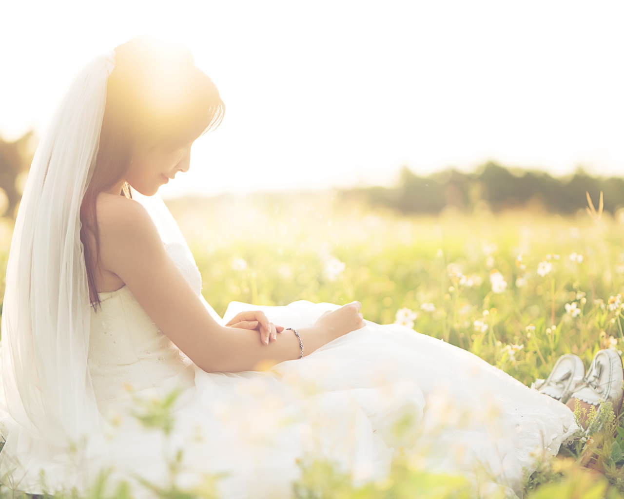 Девушка азиатка в платье невесты сидит на траве в поле 