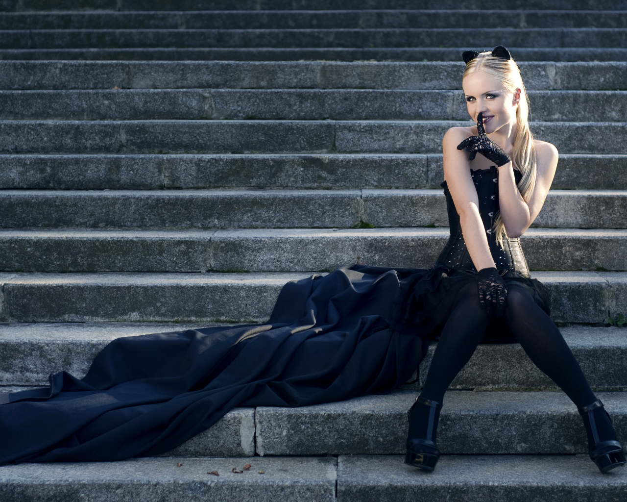 Красивая девушка блондинка  сидит на ступеньках в черном костюме