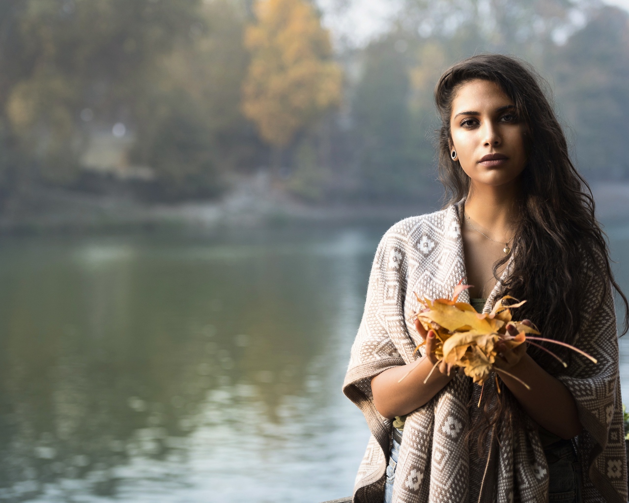 Красивая брюнетка у реки с желтыми листьями в руках