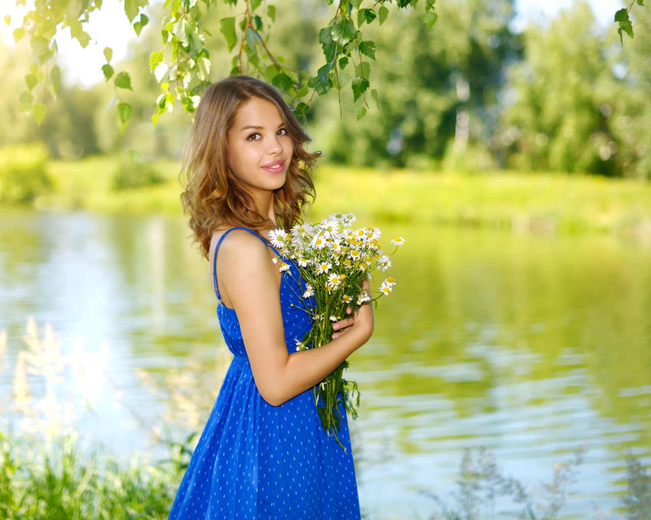Красивая девушка шатенка в синем сарафане с букетом ромашек у воды