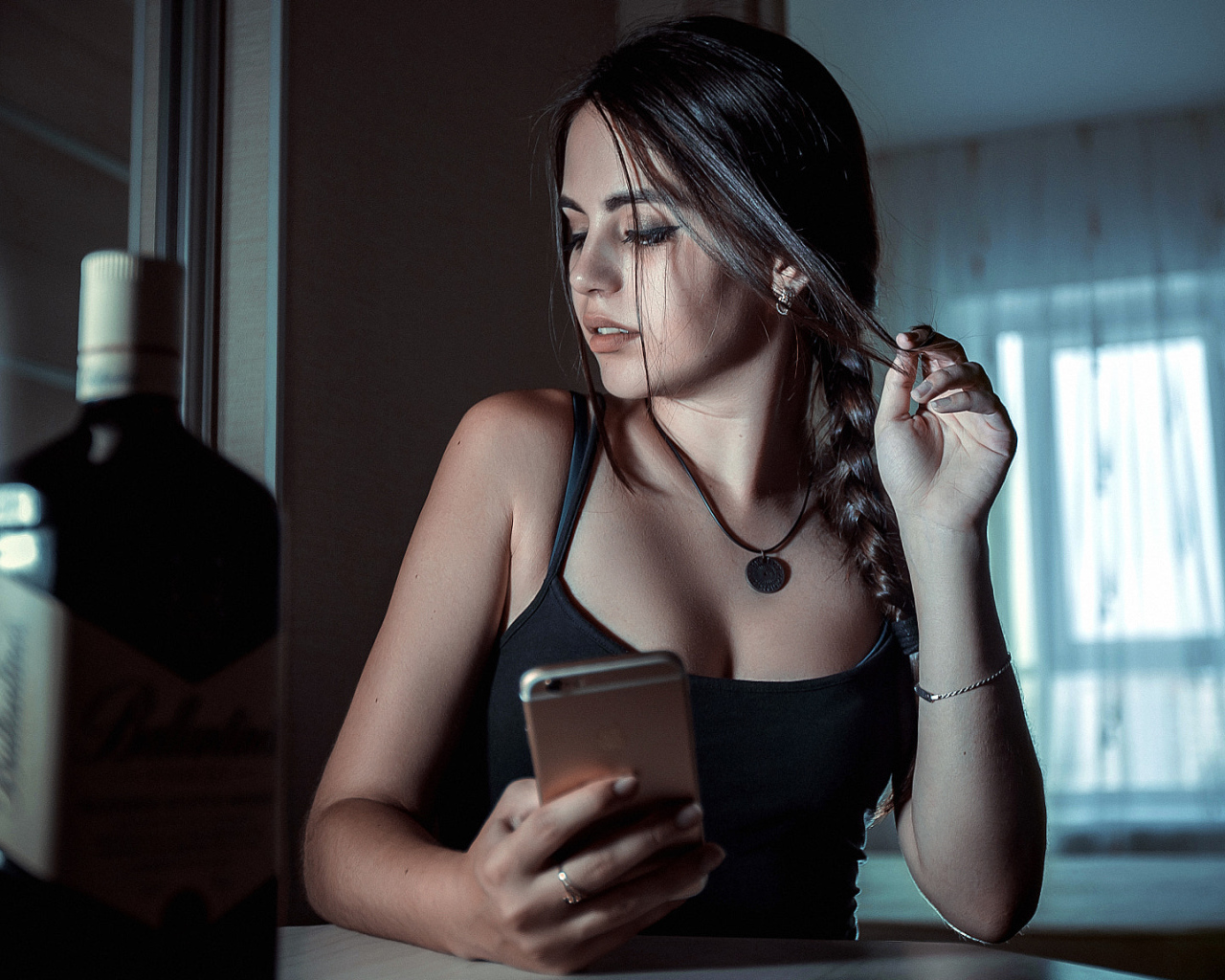 Красивая брюнетка с телефоном в руках и бутылкой