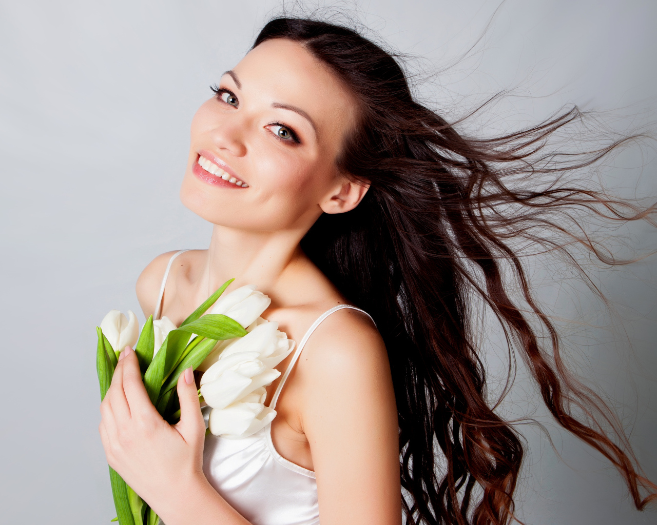 Красивая улыбающаяся брюнетка с букетом тюльпанов на сером фоне