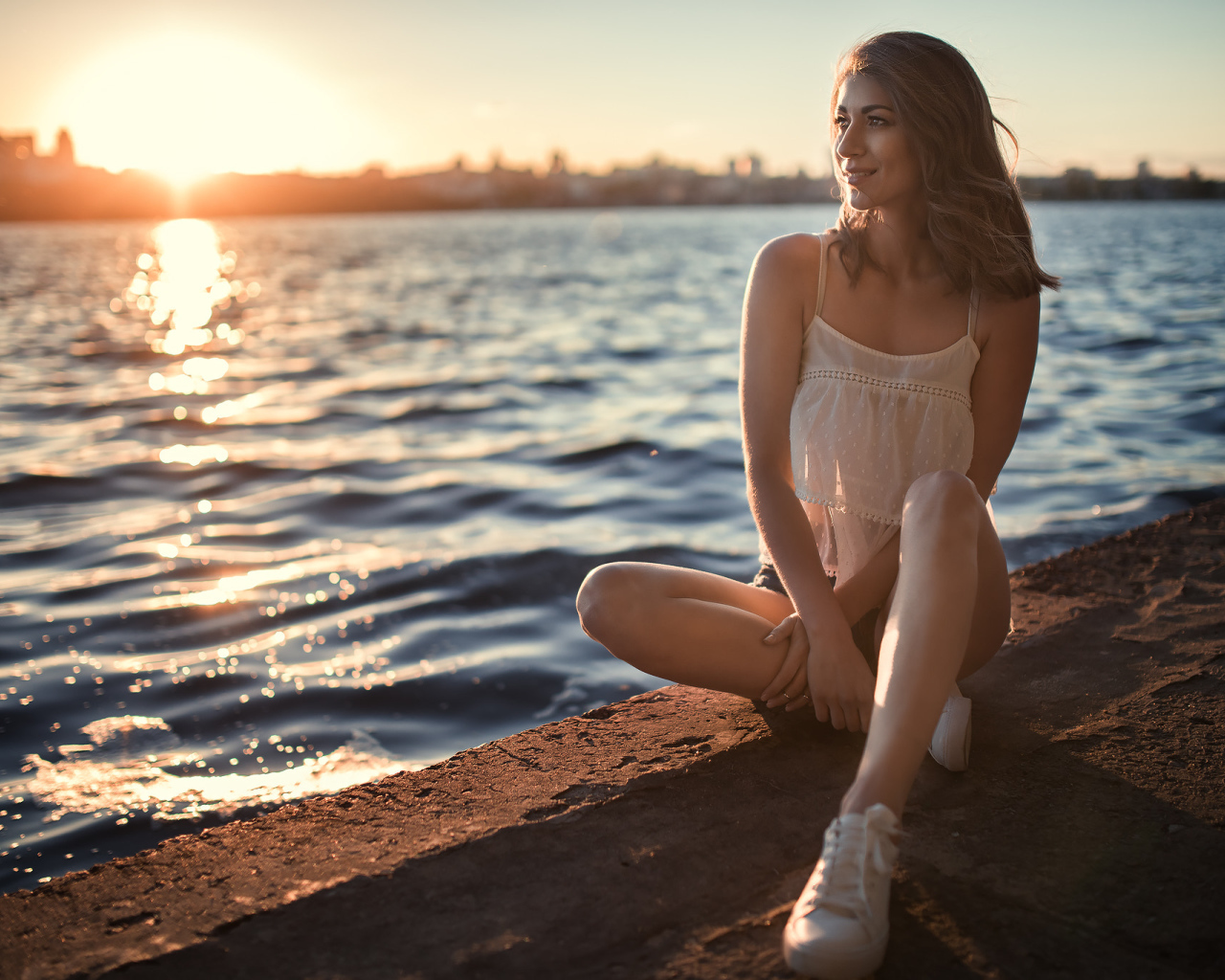 Красивая улыбающаяся девушка сидит в лучах солнца у реки