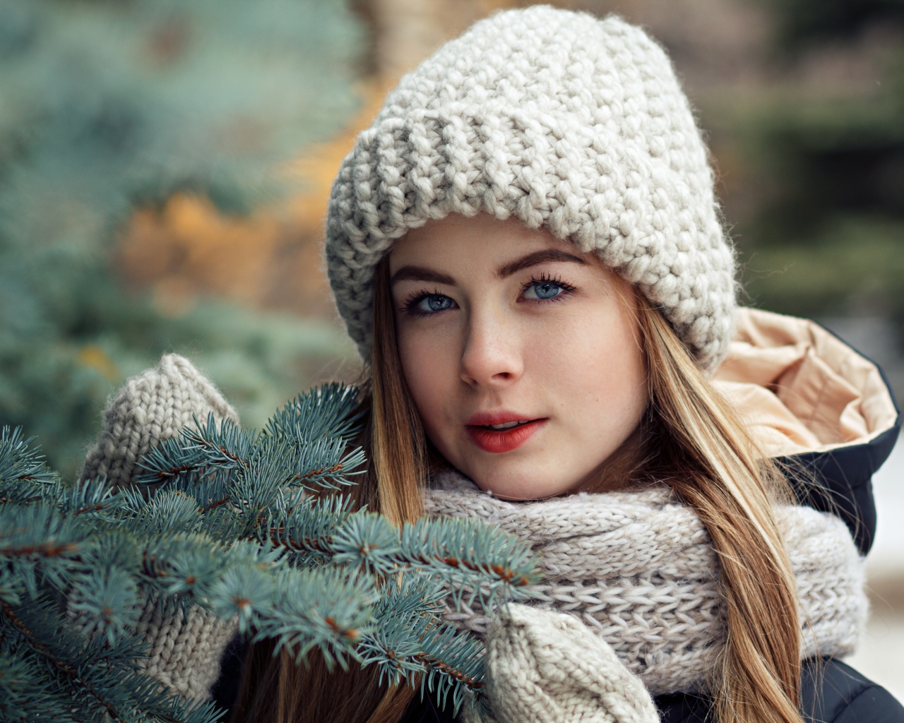 Красивая молодая голубоглазая девушка у еловой ветки зимой