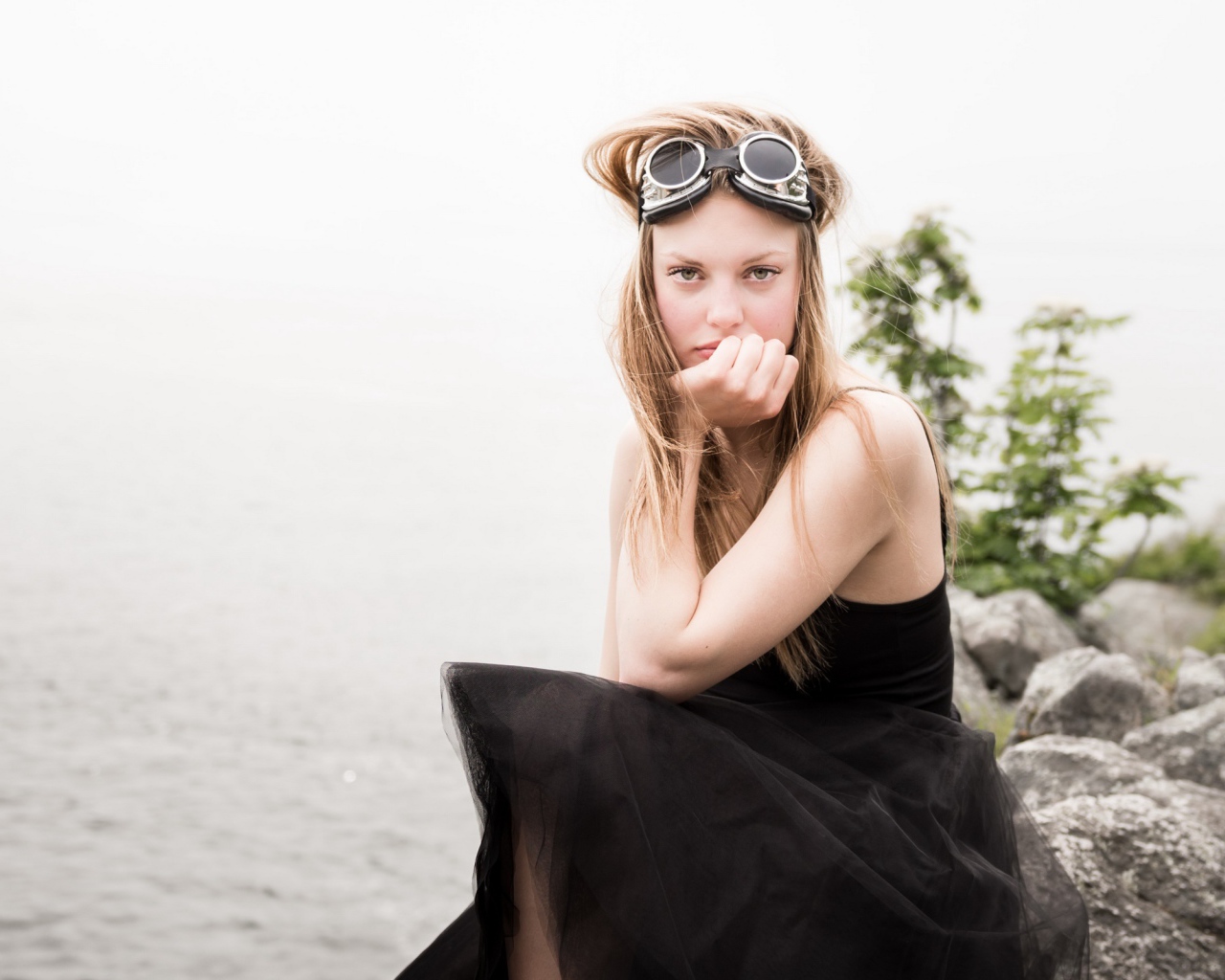 Девушка блондинка с очками на голове сидит на камне