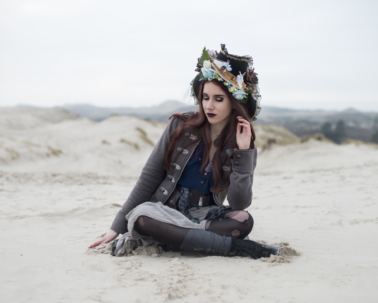 Девушка брюнетка  в костюме сидит на песке 