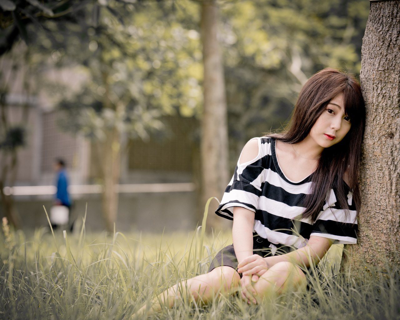 Молодая девушка азиатка сидит на траве у дерева