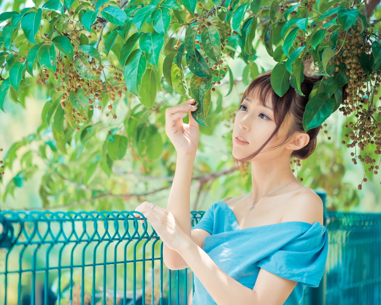 Молодая красивая девушка азиатка стоит у ветки с зелеными листьями