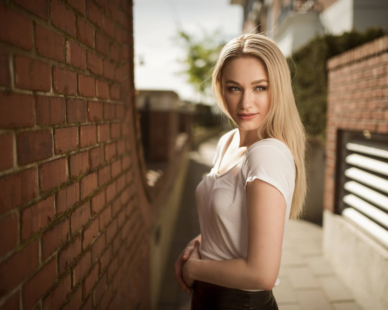 Молодая девушка блондинка у кирпичной стены 