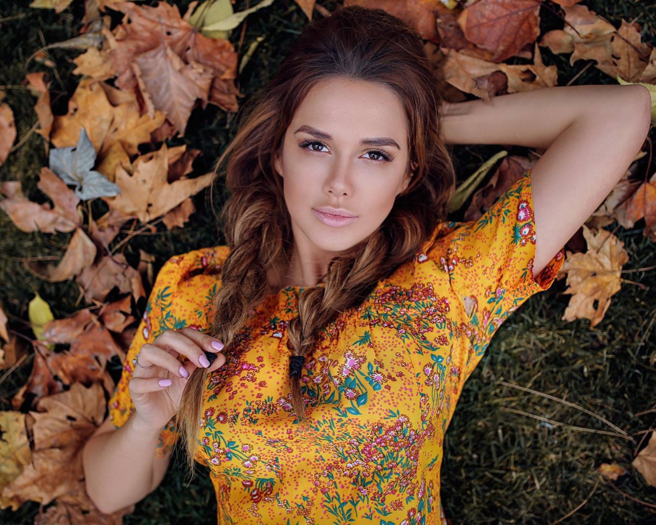 Молодая брюнетка лежит на траве с сухими листьями