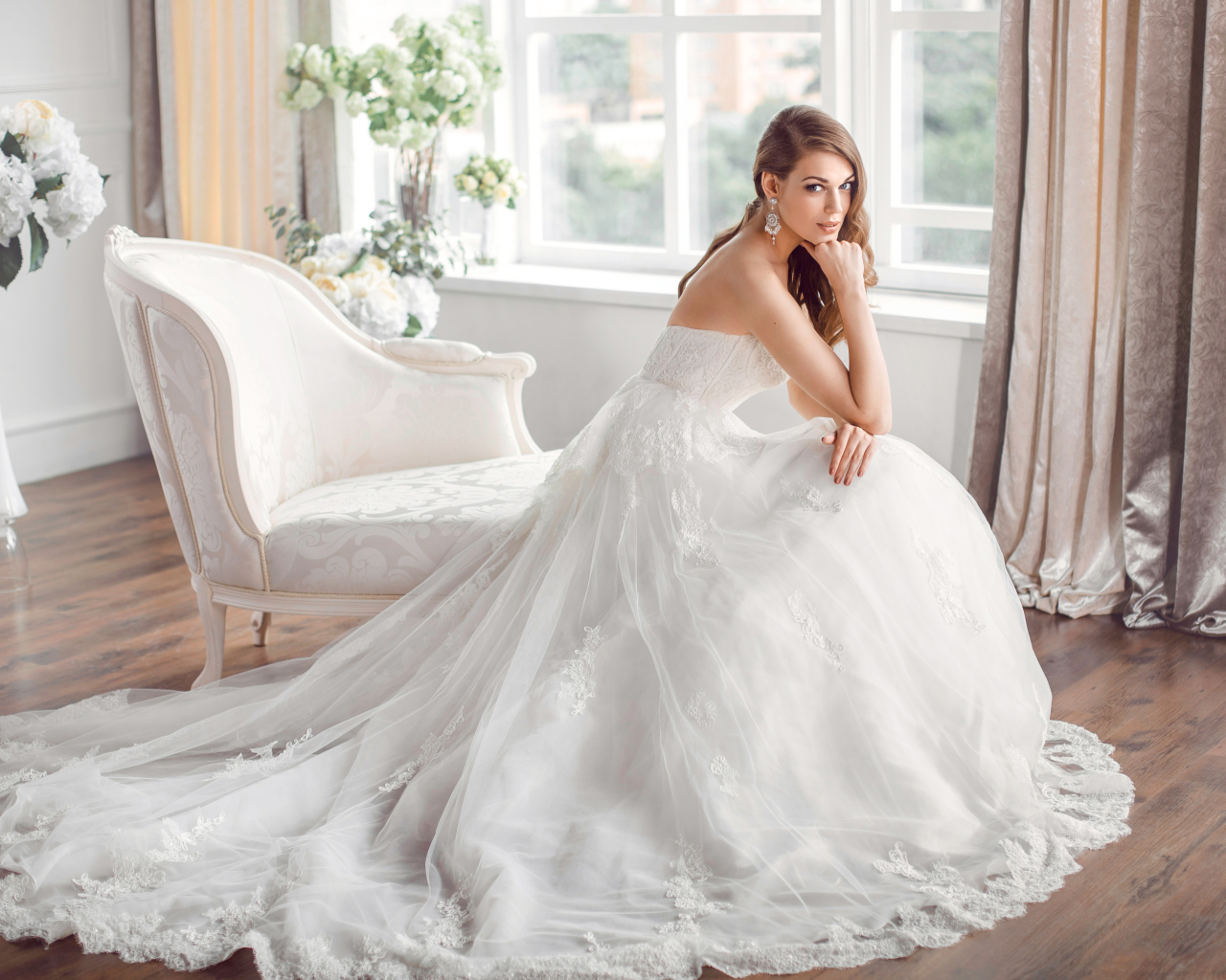 Молодая девушка в красивом свадебном платье сидит в белом кресле