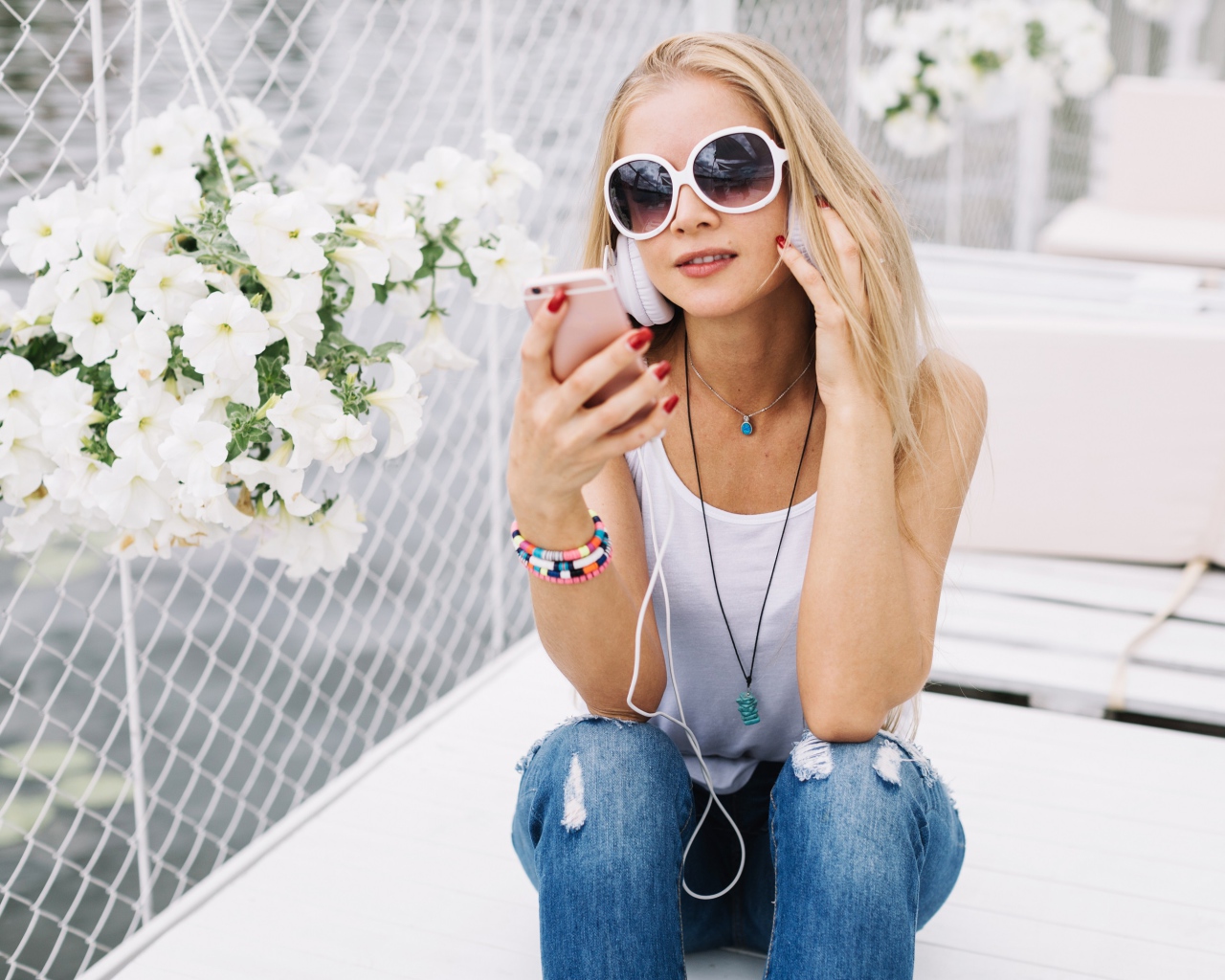 Молодая девушка в солнечных очках сидит с телефоном у белых цветов