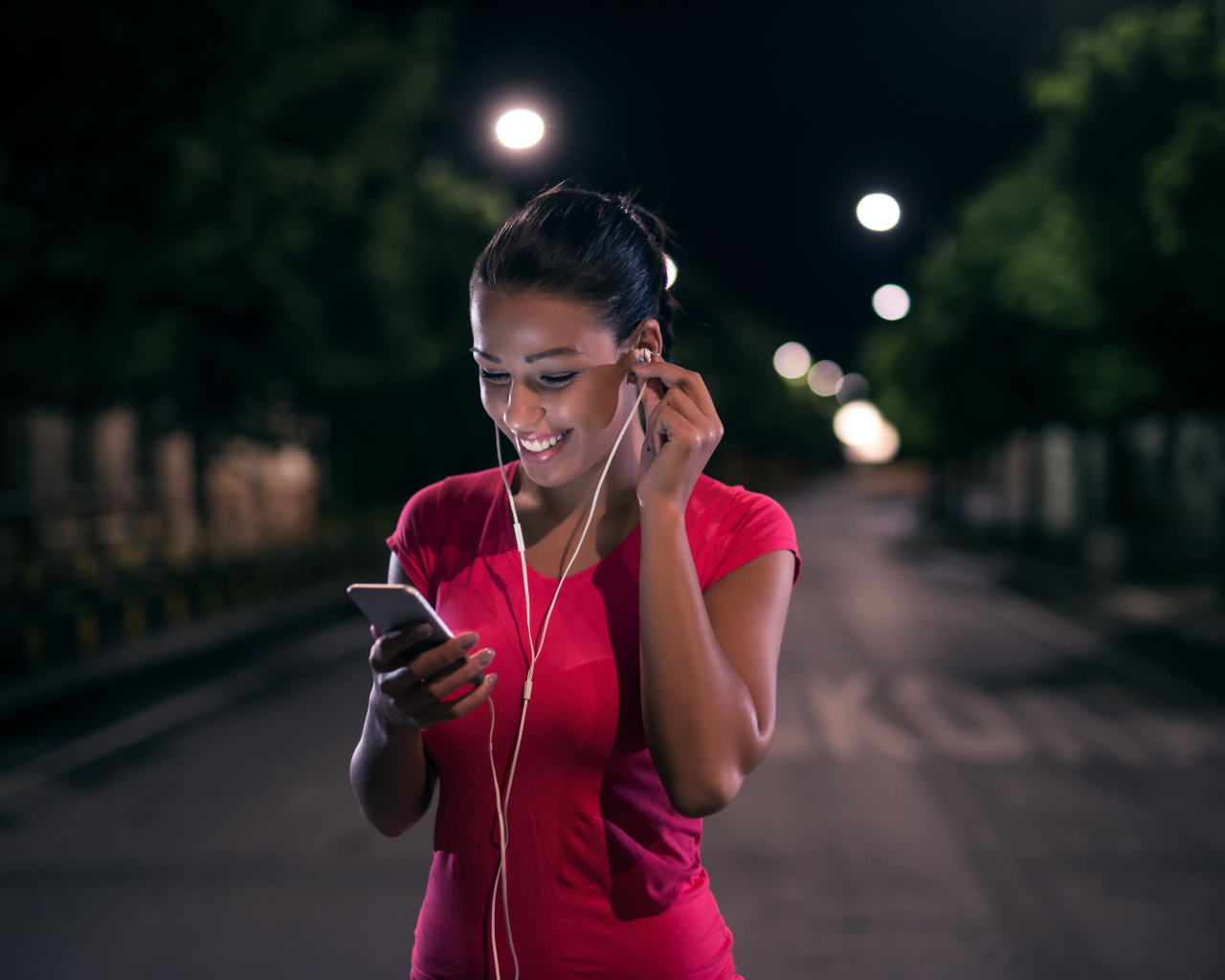 Молодая улыбающаяся девушка в наушниках с телефоном в руках