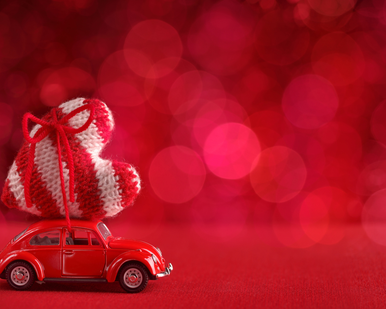 Красная игрушечная машинка везет с сердечко на розовом фоне, фон для открытки на День Святого Валентина