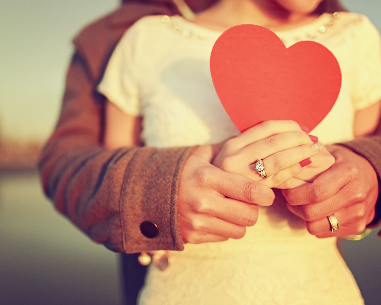 Влюбленная пара держит в руках красное бумажное сердце