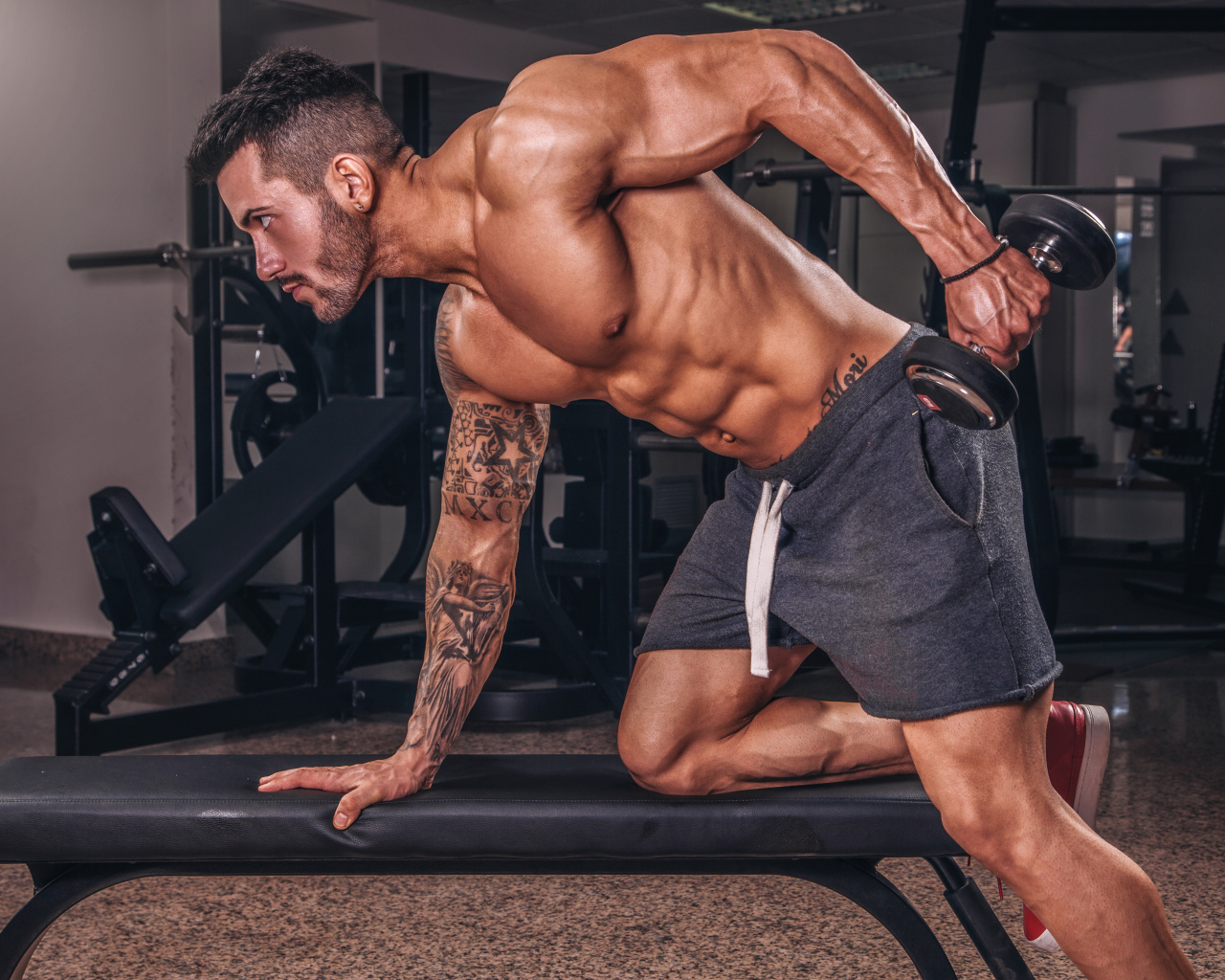 Мускулистый мужчина занимается в спортзале с гантелей