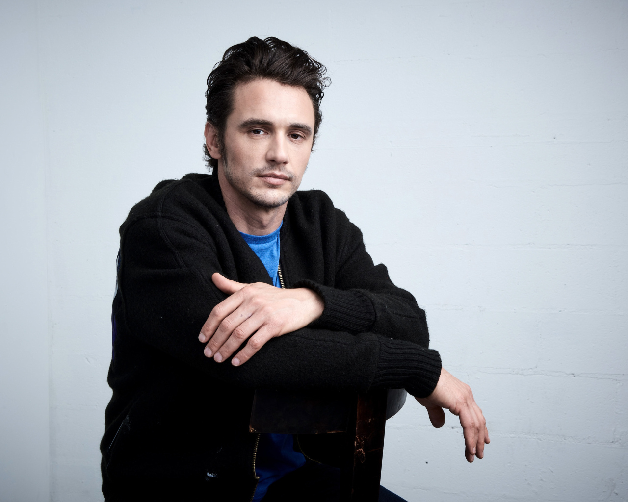 Актер Джеймс Франко в черной кофте на сером фоне