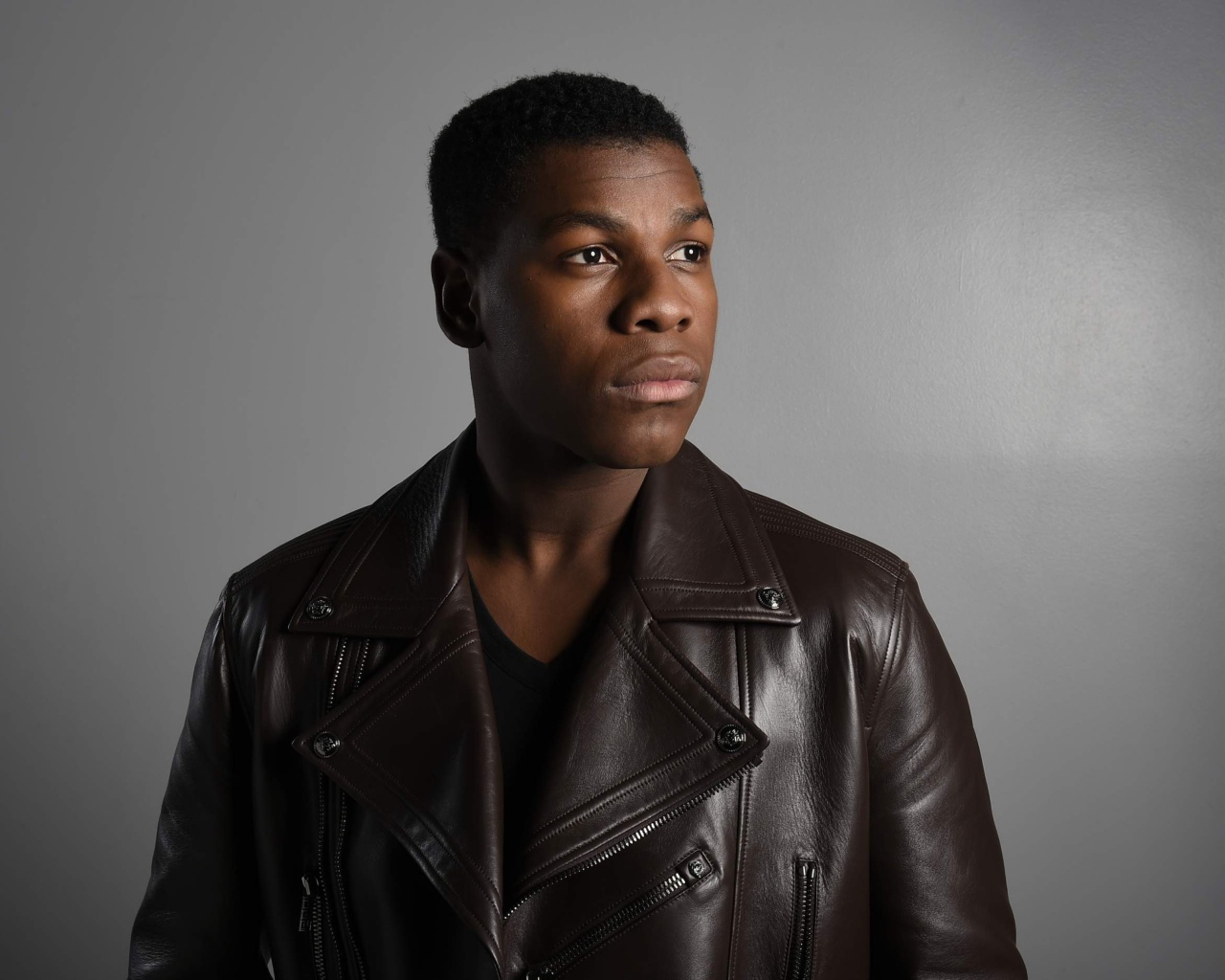 Актер  Джон Бойега в кожаной куртке на сером фоне