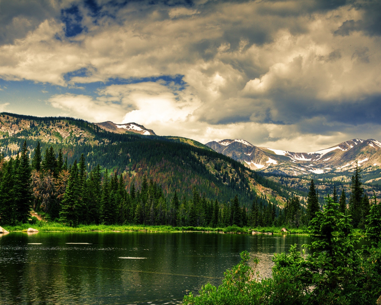 Чистое горное озеро на фоне покрытых лесом гор под облачным небом