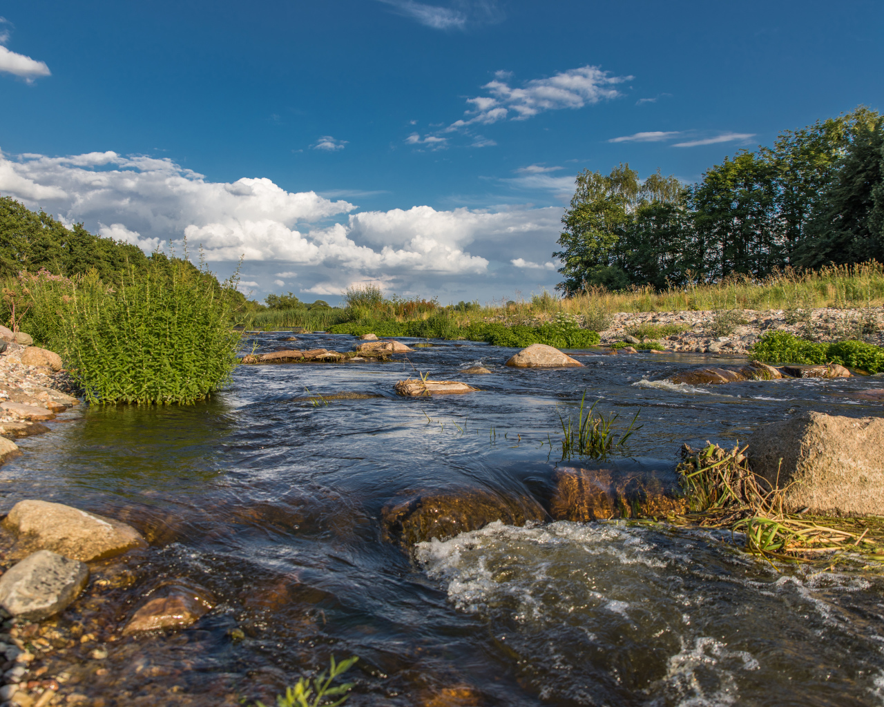 Быстрая речная вода стекает по камням под красивым голубым небом