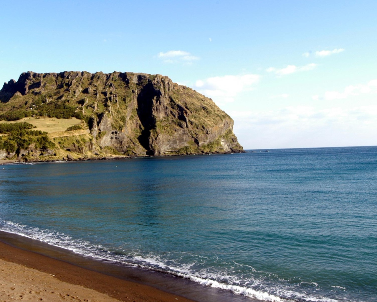 Гора на фоне спокойной воды моря под голубым небом