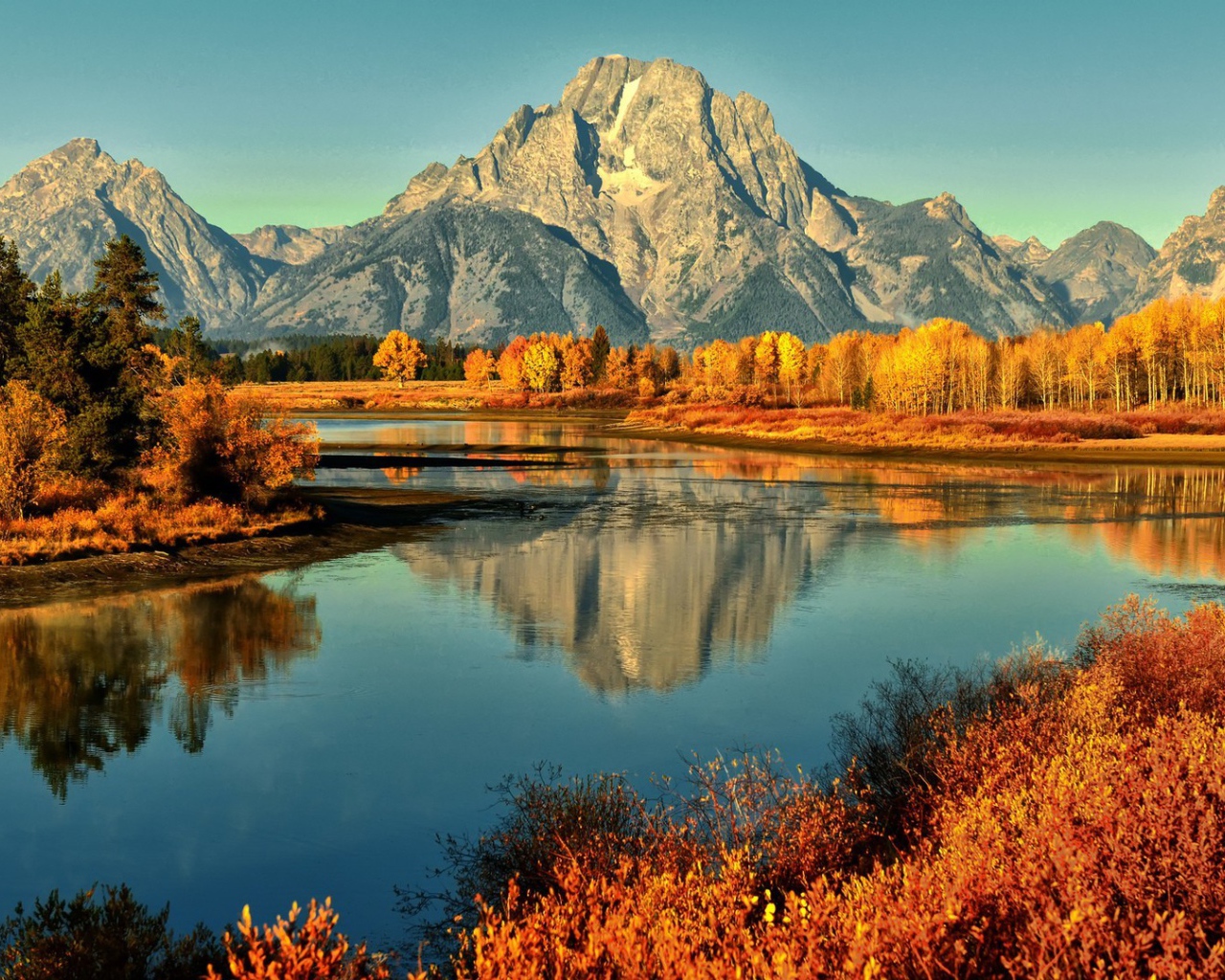 Горы и осенние деревья отражаются в реке 