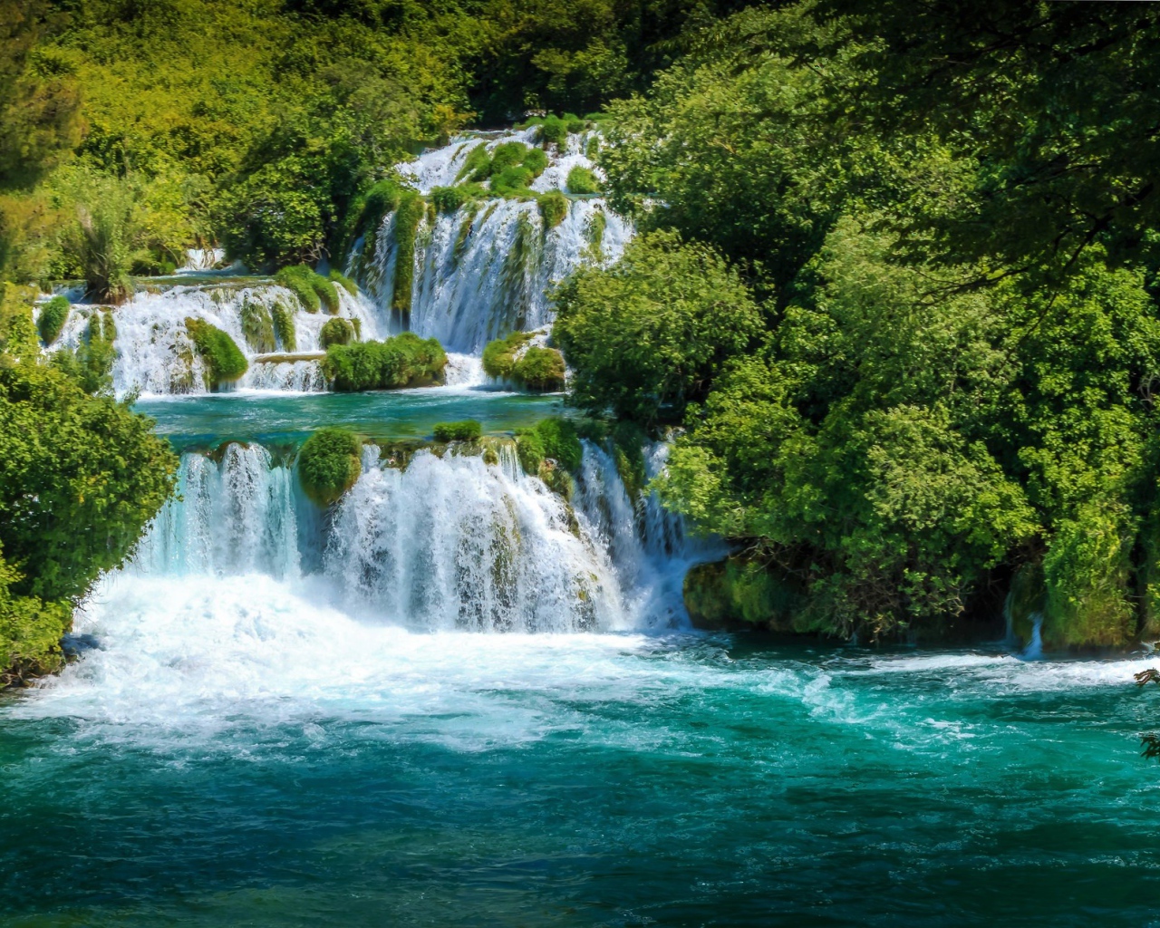 Бушующая голубая вода водопада у зеленых деревьев