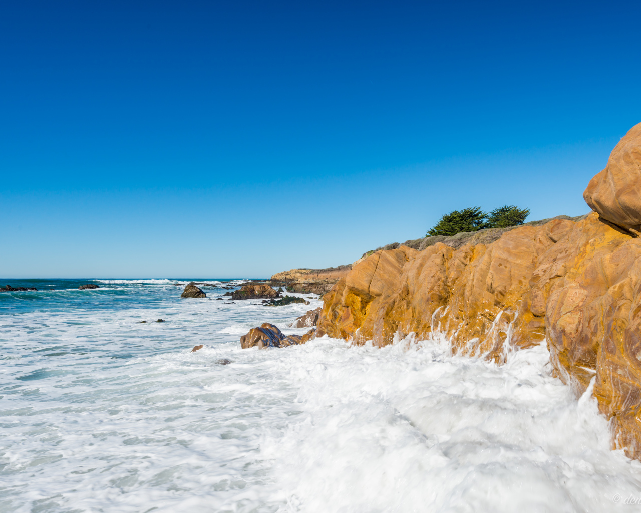 Белые волны бьются о скалы на берегу океана под голубым небом