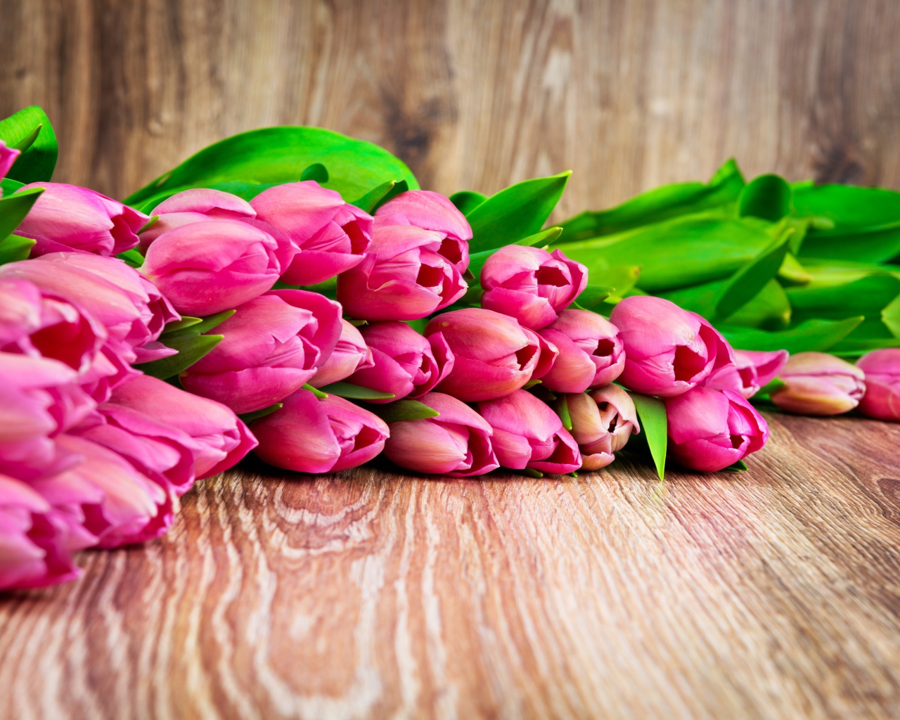 Букет розовых тюльпанов лежит на деревянной поверхности