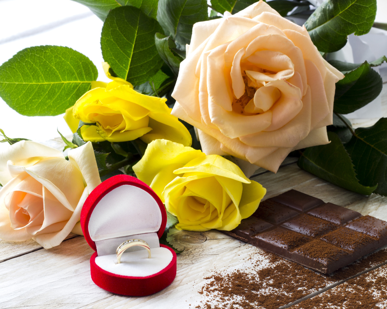 Букет роз на столе с шоколадкой и красной коробочкой с обручальным кольцом