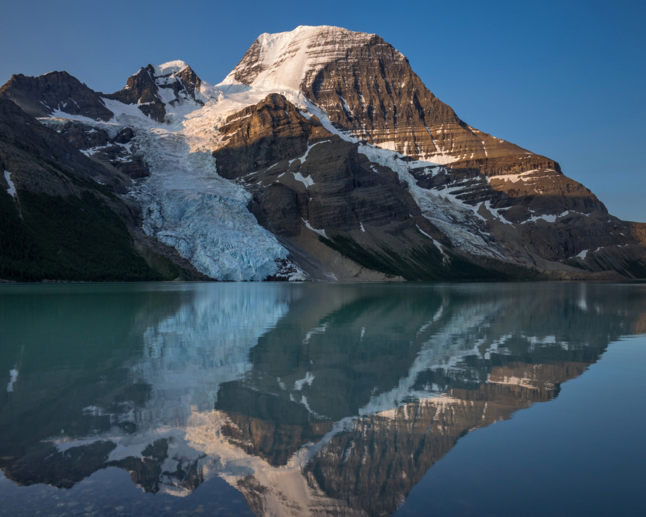 Гора в снегу отражается в водной глади озера 