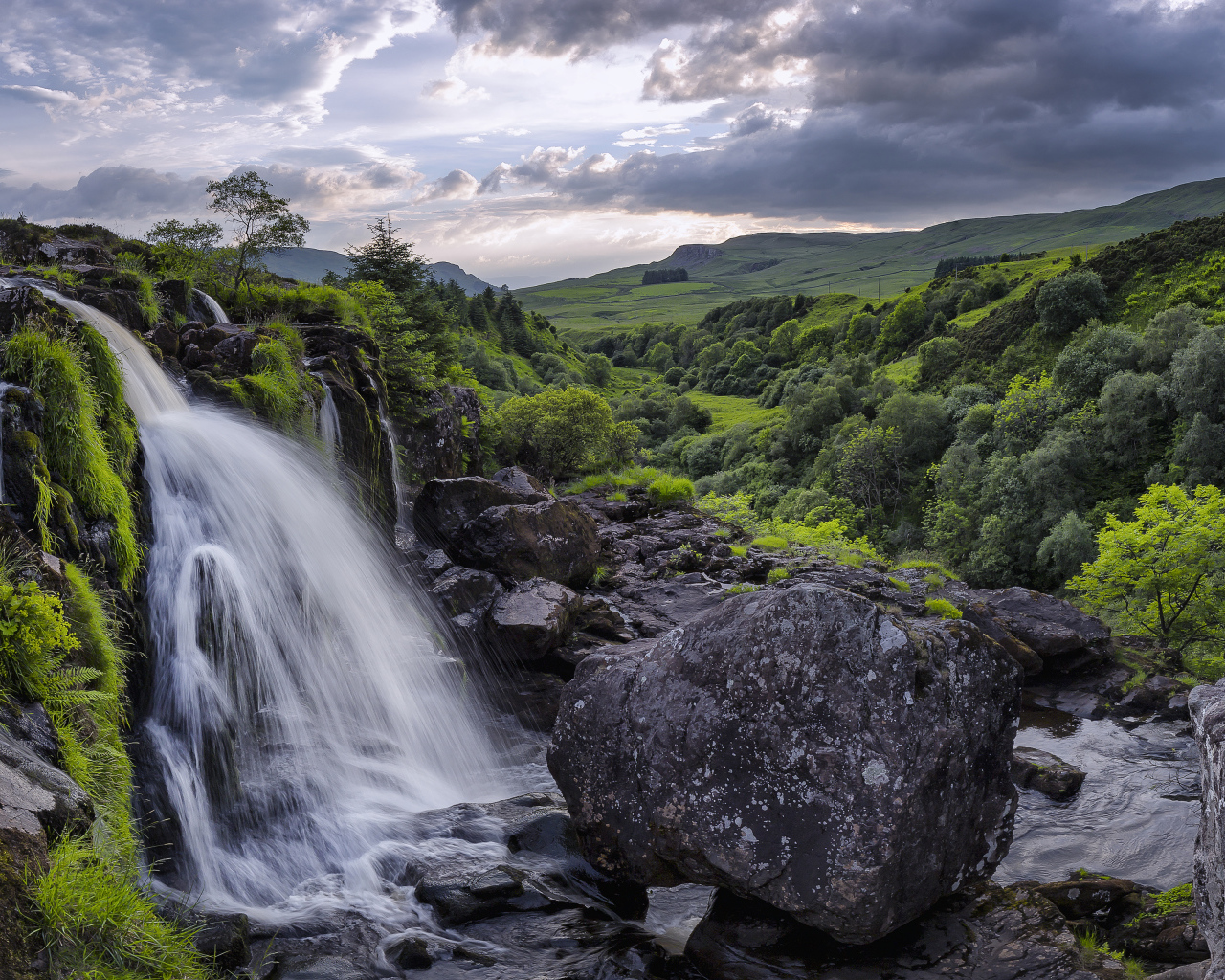 Водопад стекает по камням на фоне красивого неба и зеленого леса