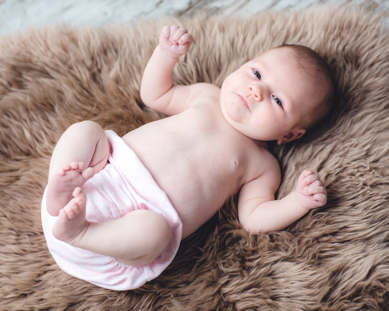 Грудной ребенок лежит на меховом покрывале