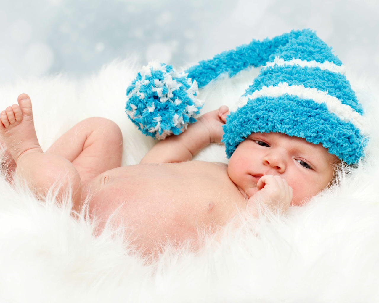Грудной ребенок в голубой шапке с бубоном на голове