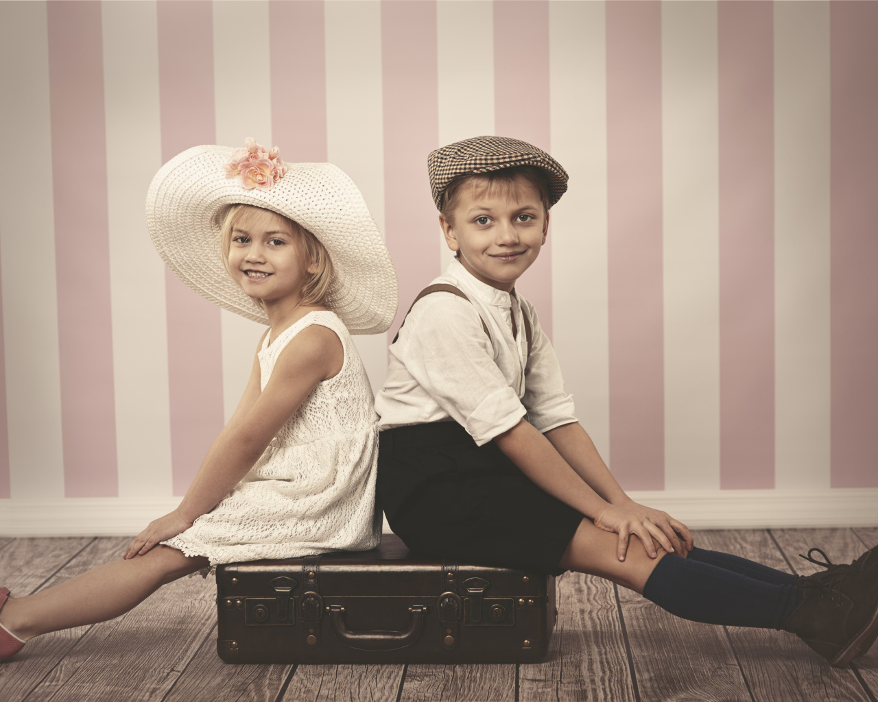 Девочка в большой белой шляпе и мальчик сидят на чемодане