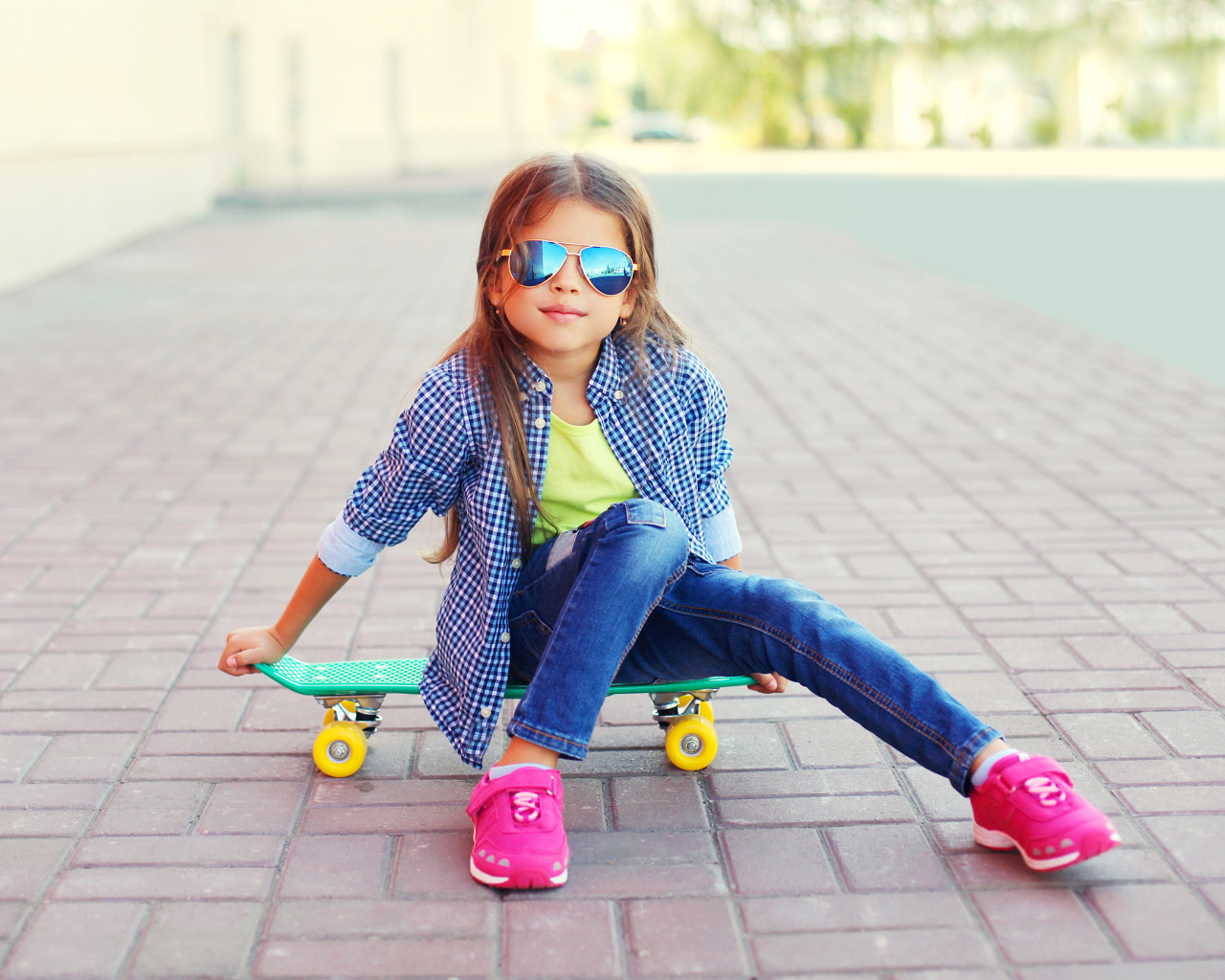 Девочка в солнечных очках сидит на скейтборде