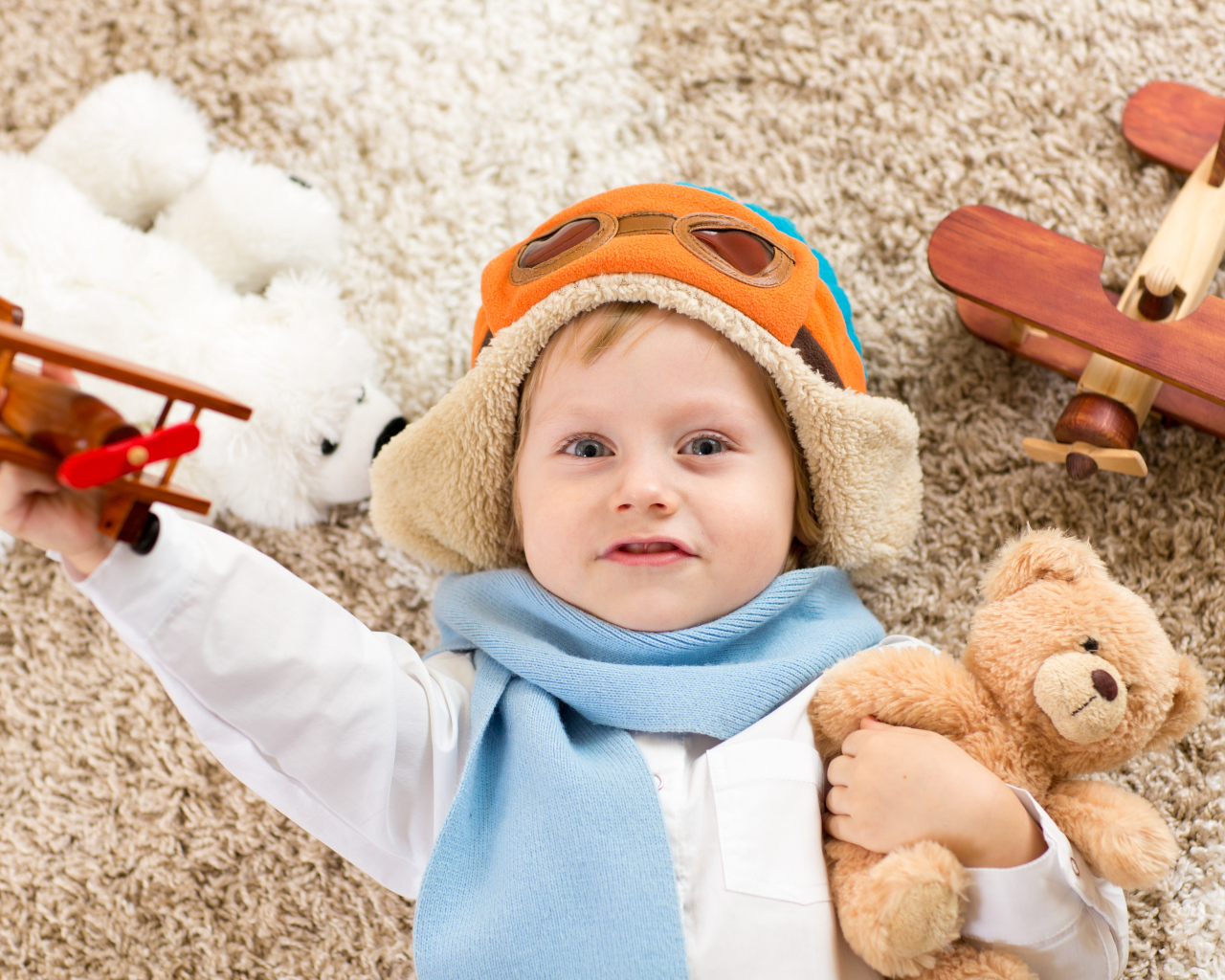 Маленький мальчик в шапке и игрушечным самолетом и медвежонком в руках