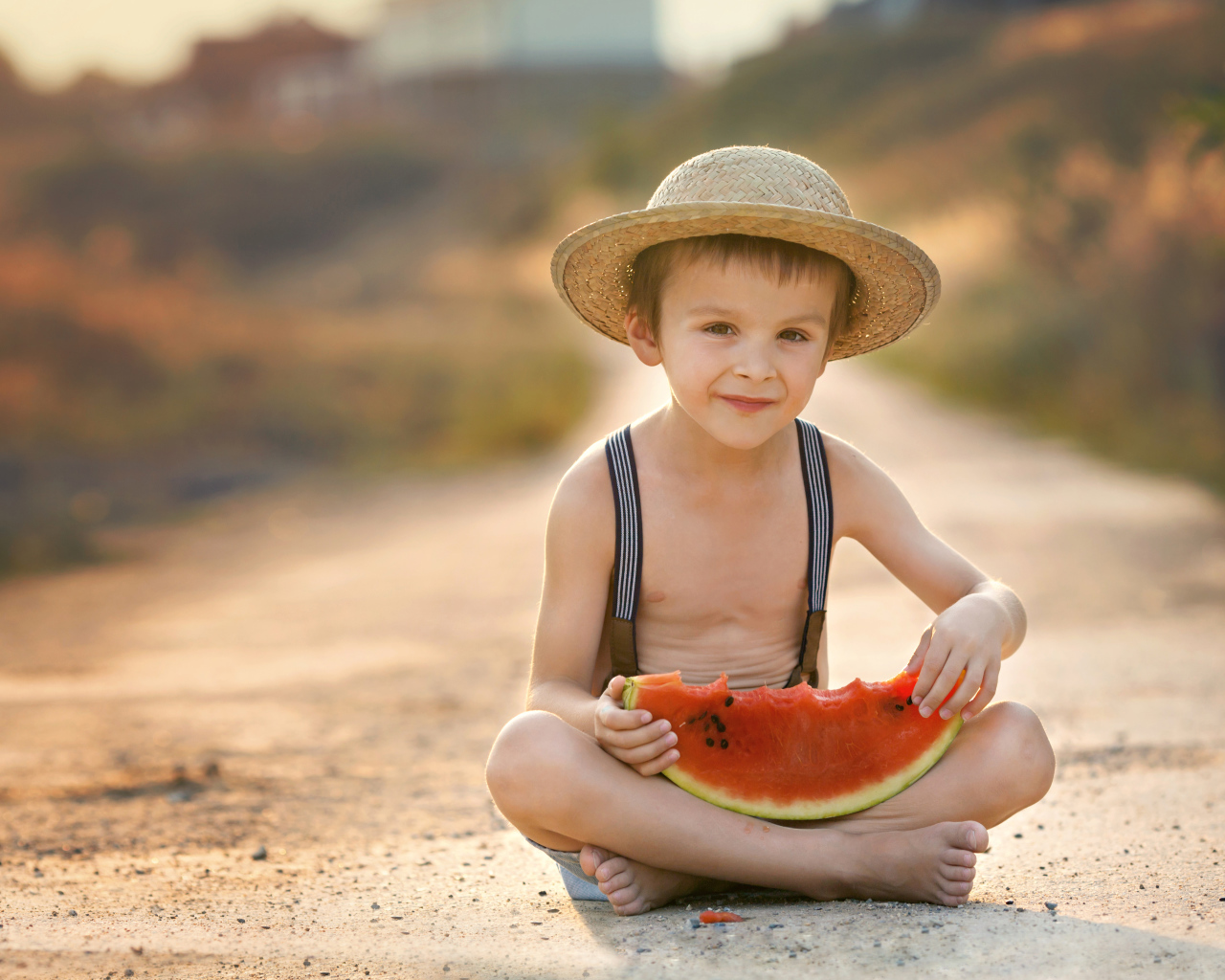 Маленький мальчик в шляпе сидит на дороге с долькой арбуза