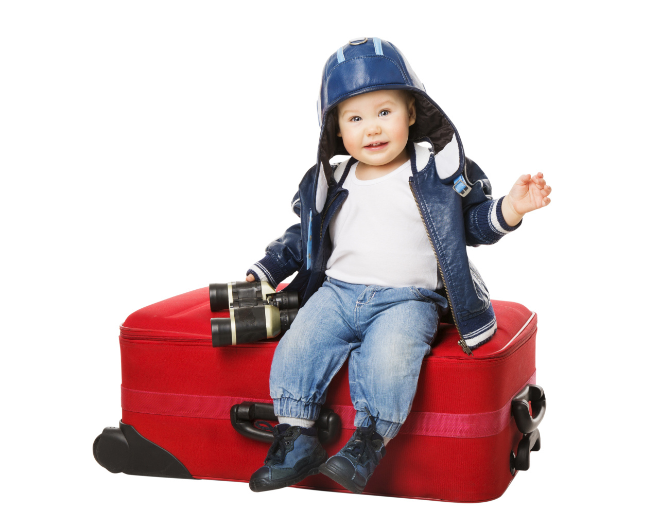 Маленький мальчик в шапке с биноклем сидит на красном чемодане