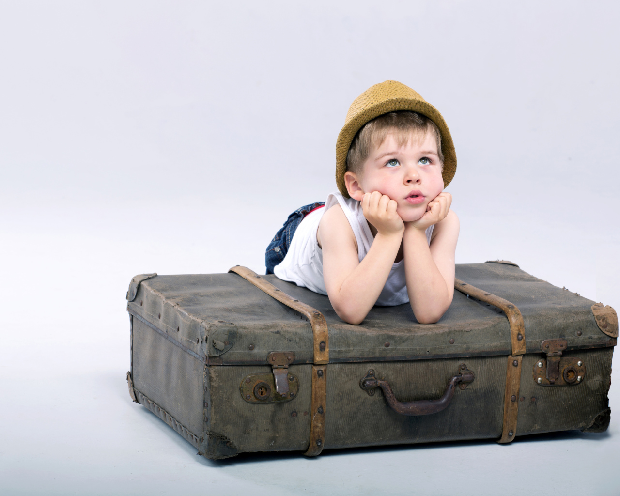 Маленький мальчик лежит на большом чемодане на сером фоне