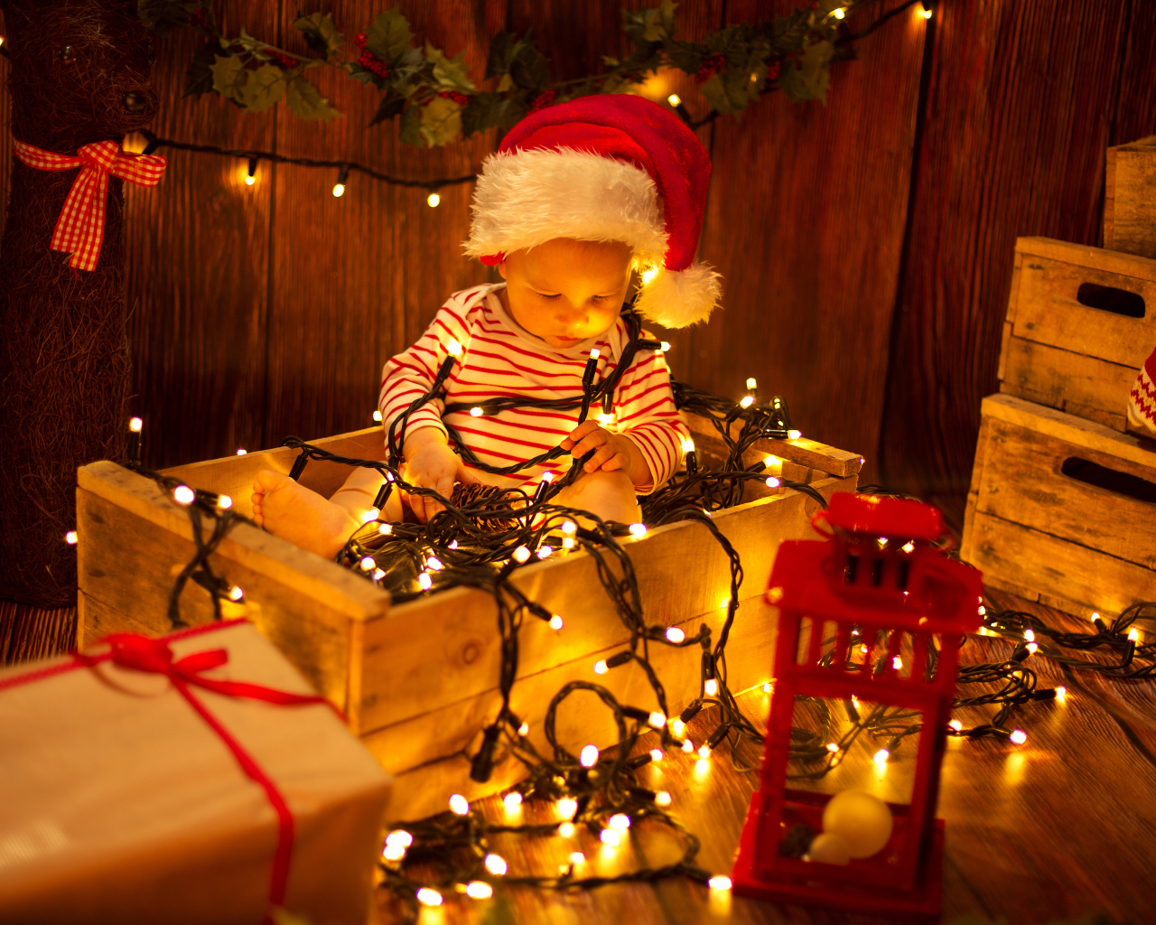 Маленький мальчик сидит в коробке с новогодней гирляндой