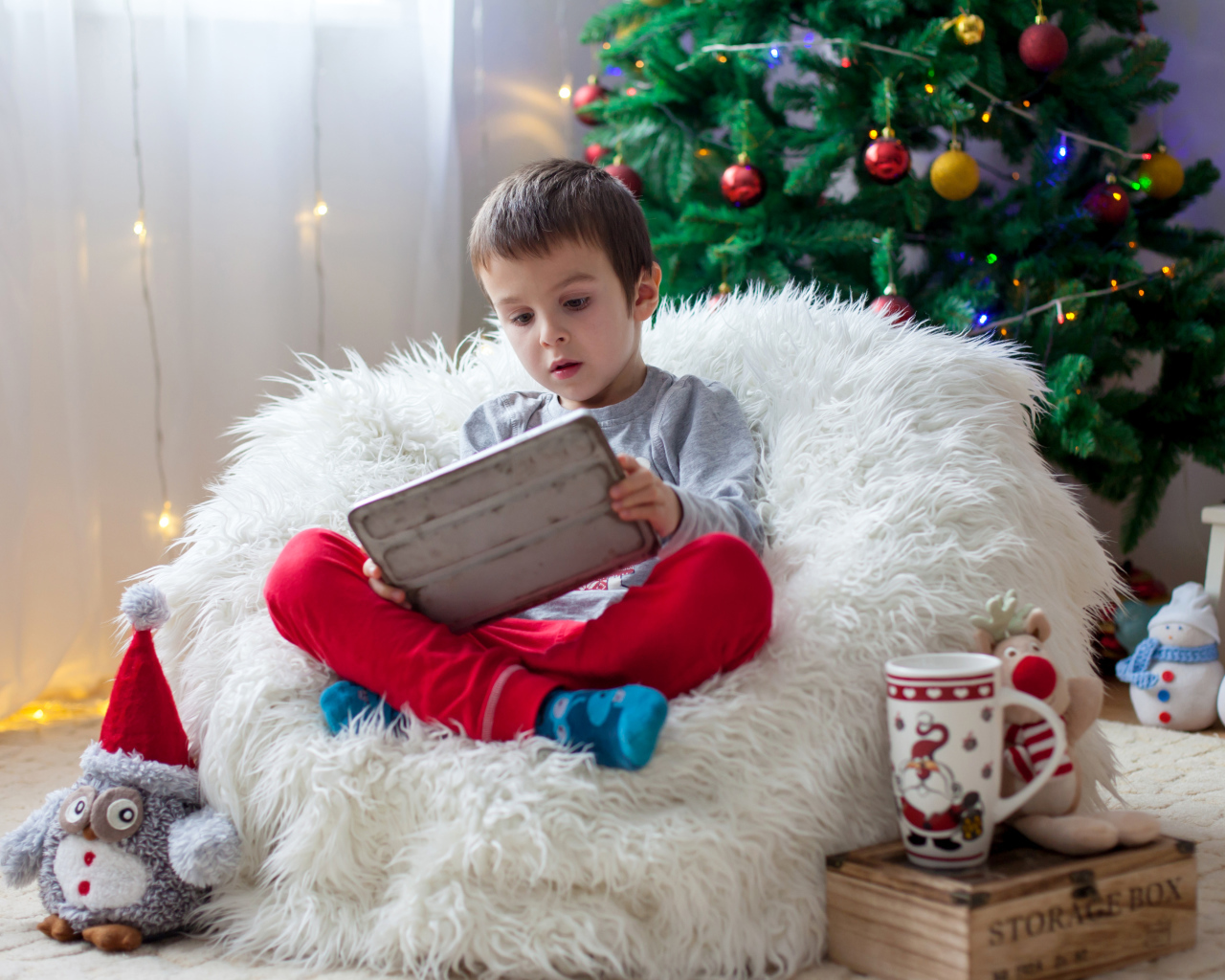 Маленький мальчик сидит в мягком кресле у новогодней елки
