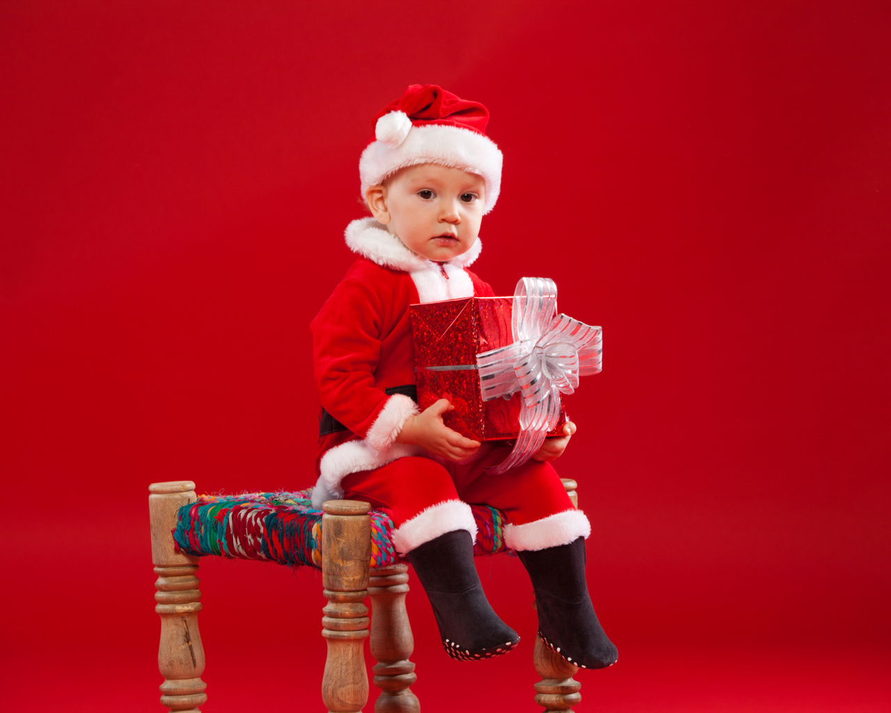 Маленький мальчик сидит на стуле с новогодним подарком