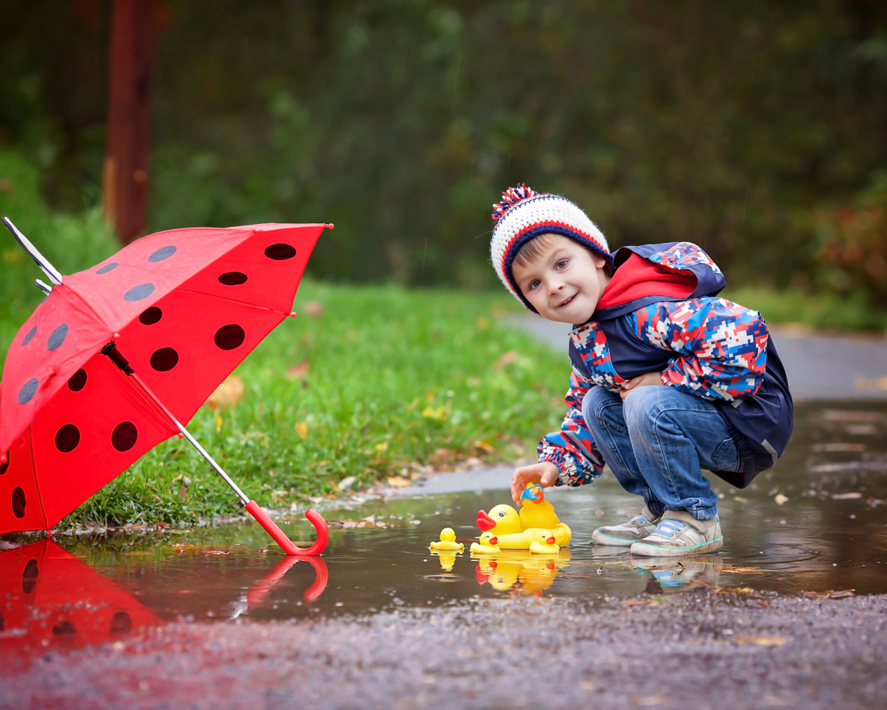 Маленький мальчик пускает резиновую уточку в лужу после дождя
