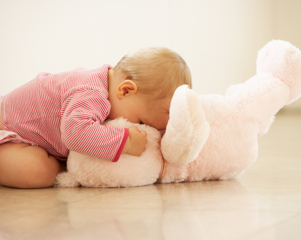 Маленький ребенок играет с розовым плюшевым мишкой