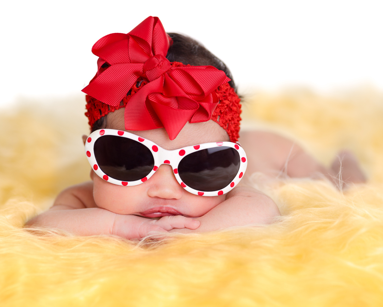 Маленькая забавная малышка в очках и с красным бантом на голове