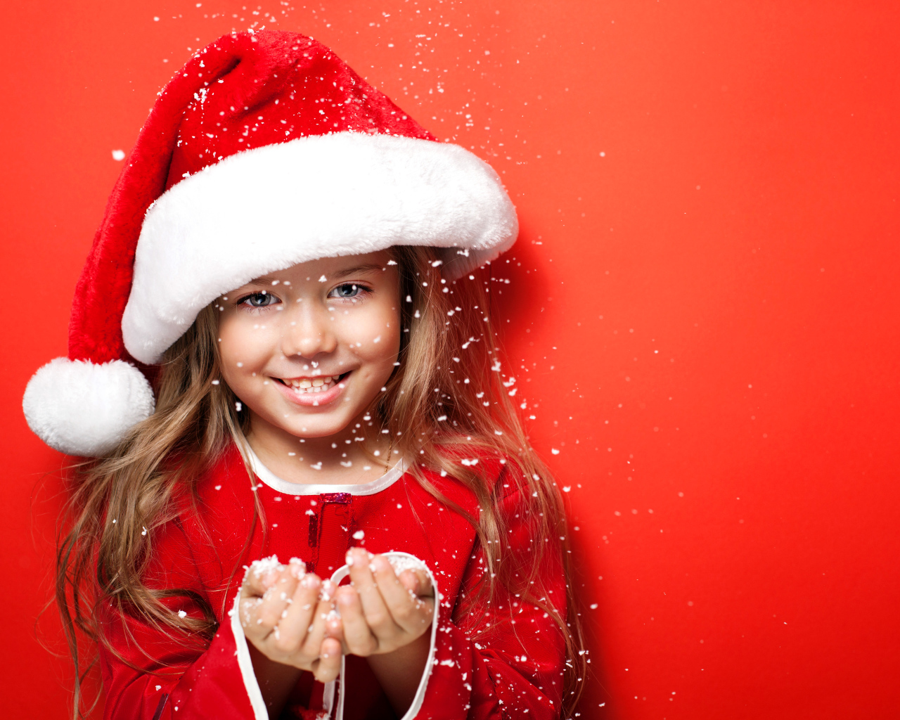 Маленькая девочка в новогодней шапке ловит руками снежинки